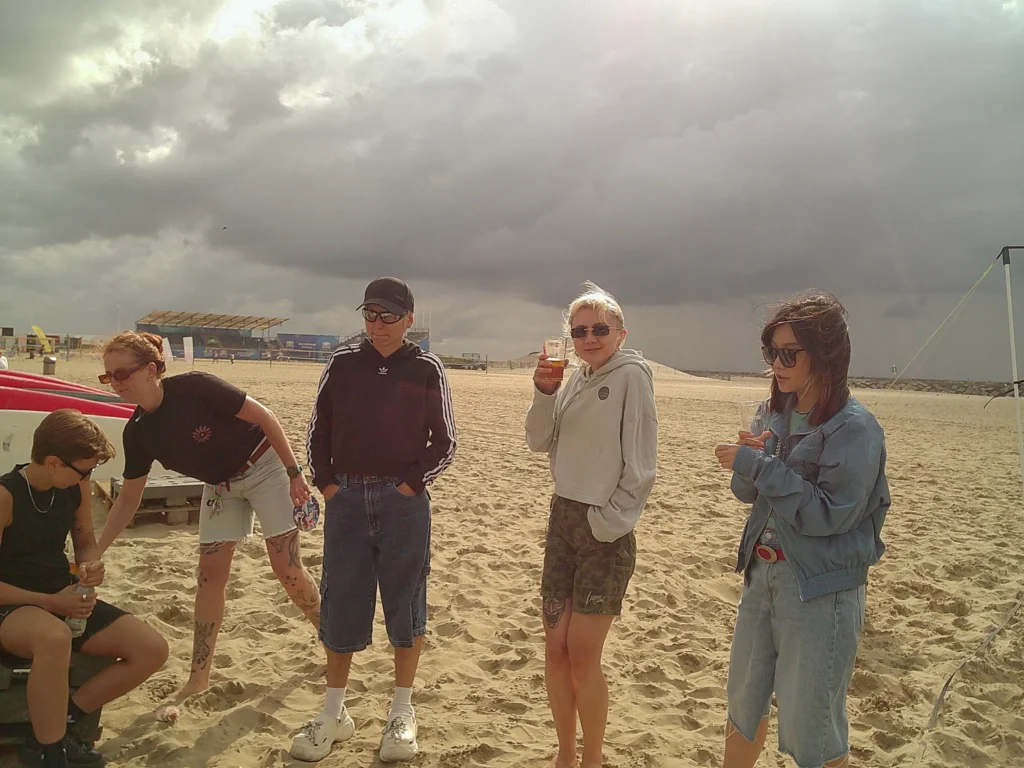 Five people gathered on the beach wearing summer clothes, the sky is grey